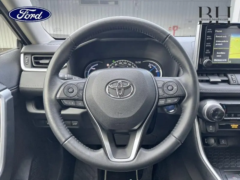 Vue intérieure centrée sur le volant cuir multifonction d'un Toyota RAV4 2.5 Hybride 2022, avec tableau de bord et écran tactile visibles.