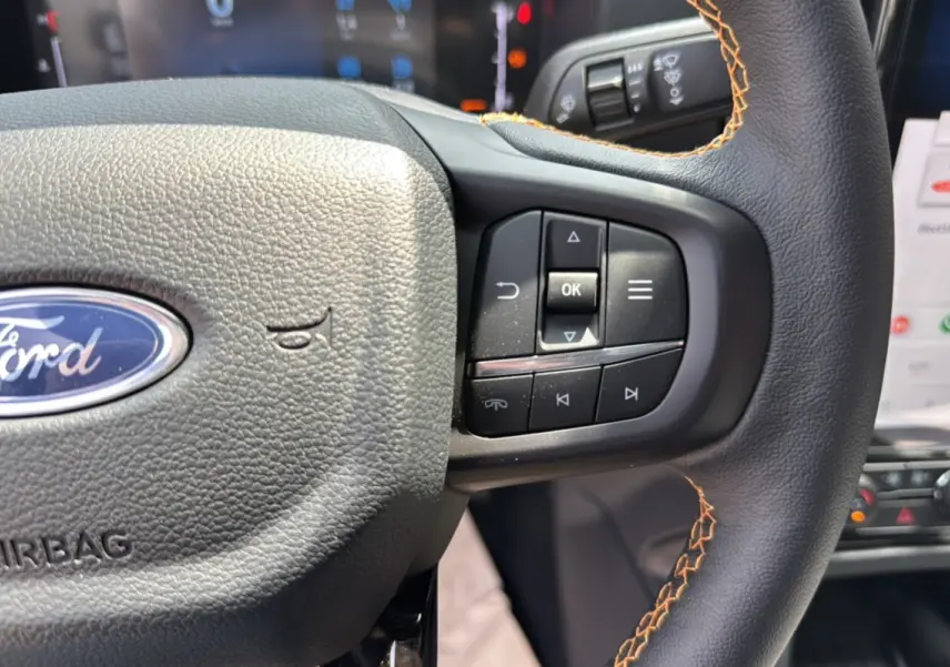 Gros plan sur le volant cuir noir avec surpiqûres orange du Ford Ranger Wildtrak 2026, boutons multifonctions visibles.