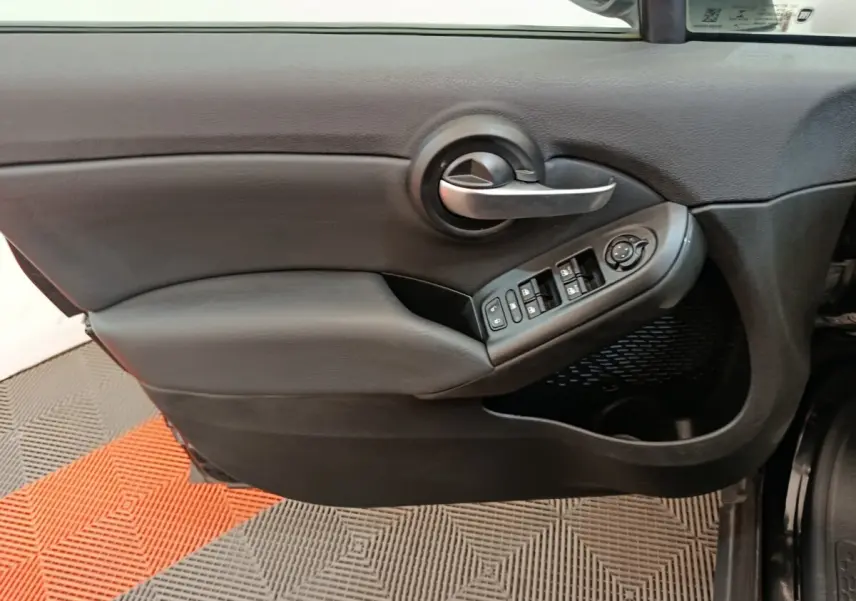 Gros plan sur la porte intérieure côté conducteur noire de la Fiat 500X avec commandes des vitres et poignée argentée.