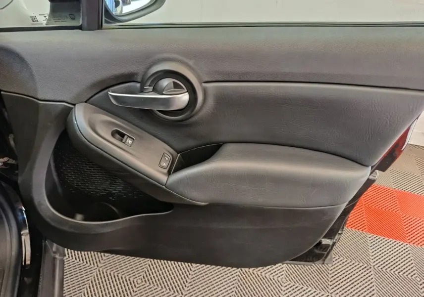 Gros plan sur la porte intérieure côté conducteur noire de la FIAT 500X avec poignée argentée et commandes électriques.