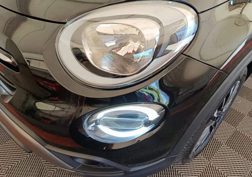Gros plan sur le phare avant droit et le feu antibrouillard d’un Fiat 500X noir, détails chromés visibles.