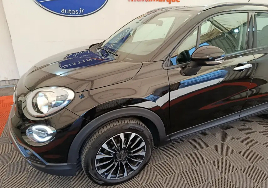 Vue 3/4 avant droit d'une FIAT 500X noire avec jantes noires et détails chromés sur les rétroviseurs et poignées.