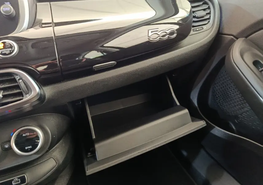 Gros plan sur la boîte à gants ouverte et le tableau de bord noir brillant avec logo 500 dans une Fiat 500X blanche.