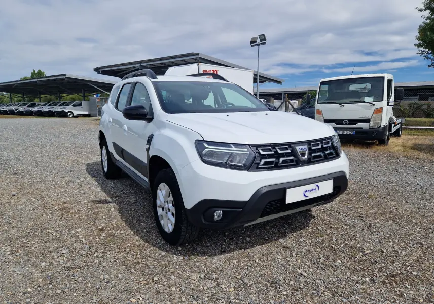 Dacia Duster blanc en 3/4 avant droit, SUV compact avec calandre noire et protections latérales noires.
