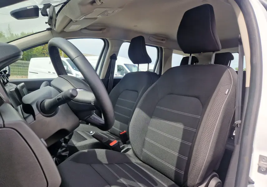Vue intérieure côté conducteur du Dacia Duster blanc 2022, montrant les sièges noirs et le volant avec boîte manuelle.