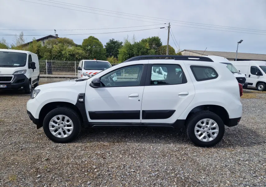 Vue de profil côté gauche d'un Dacia Duster blanc 4x4 avec protections noires et jantes alliage 16 pouces.
