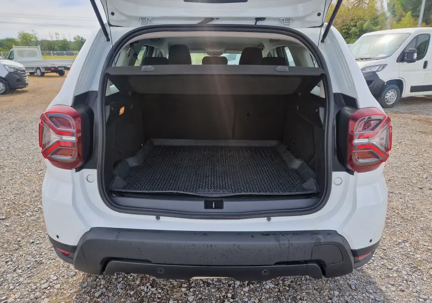 Vue arrière du coffre ouvert d'un Dacia Duster blanc 2022, avec tapis de protection et hayon relevé.