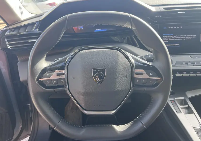 Vue rapprochée du volant multifonction noir de la Peugeot 308 2024 avec tableau de bord et écran tactile en arrière-plan.