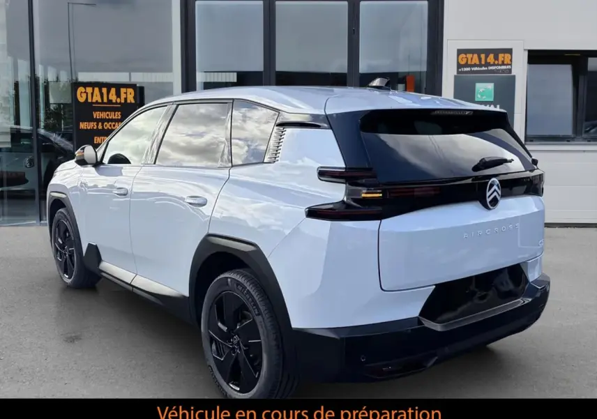Vue 3/4 arrière droite du Citroën C5 Aircross blanc avec toit noir et jantes noires devant un bâtiment.