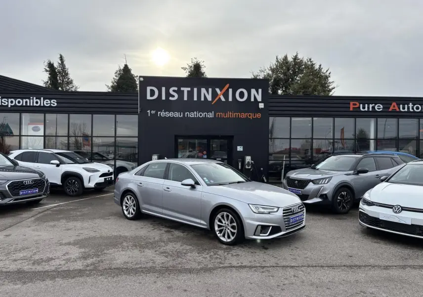 Audi A4 argent fleuret métal vue 3/4 avant droit sur parking devant concession Distinxion