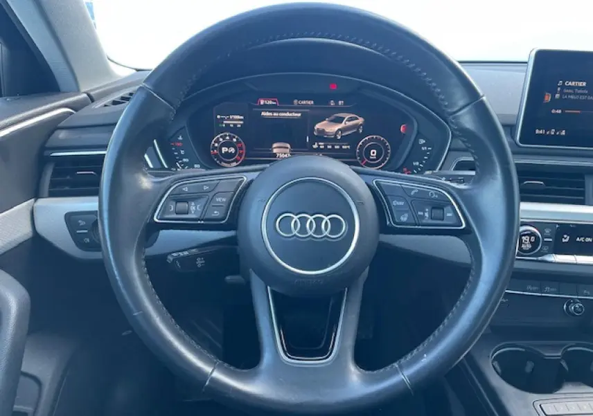 Vue intérieure centrée sur le volant cuir noir multifonction de l'Audi A4 2019 avec tableau de bord numérique.
