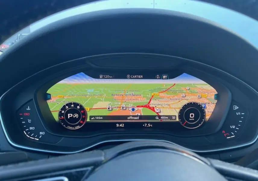Vue rapprochée du tableau de bord numérique d'une Audi A4 argent, affichant la navigation GPS en plein écran.