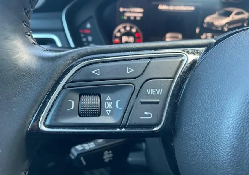 Gros plan sur les commandes multifonctions à gauche du volant cuir noir de l'Audi A4 argent Fleuret Metal 2019.
