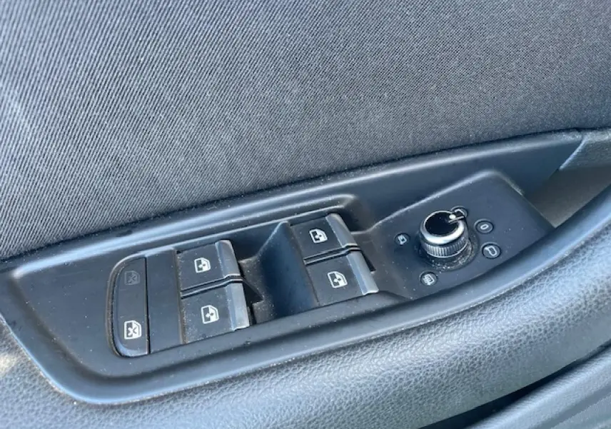 Gros plan sur les commandes de lève-vitres et réglage des rétroviseurs côté gauche d'une Audi A4 argent 2019.