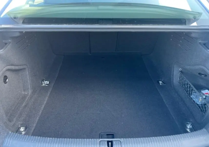 Coffre ouvert d'une Audi A4 argent fleuret métal, montrant les quatre œilletons de fixation et un filet de rangement latéral.
