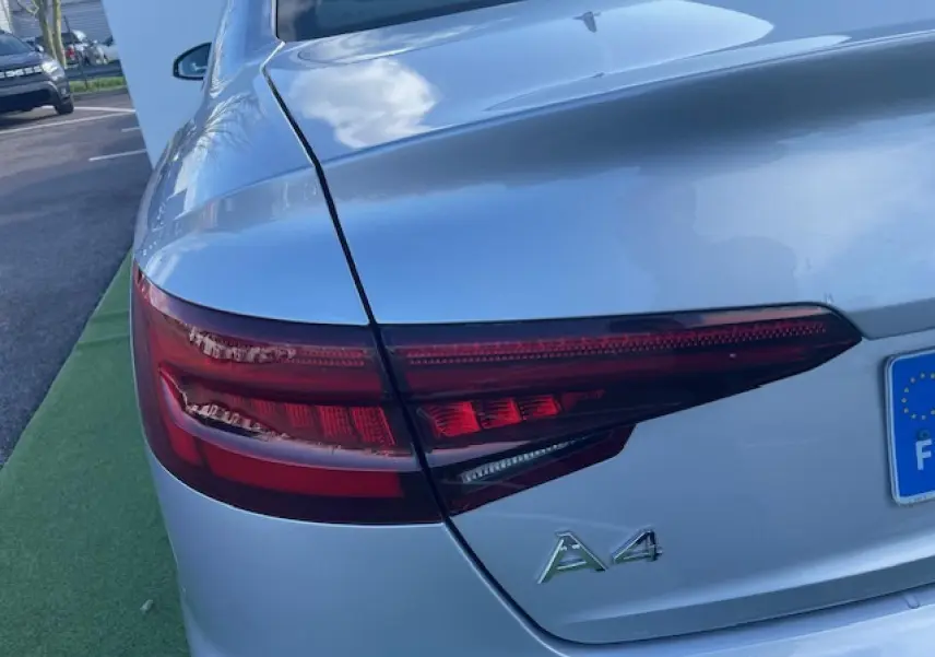 Gros plan sur le feu arrière gauche d'une Audi A4 argent fleuret métal avec logo A4 visible sur le coffre.
