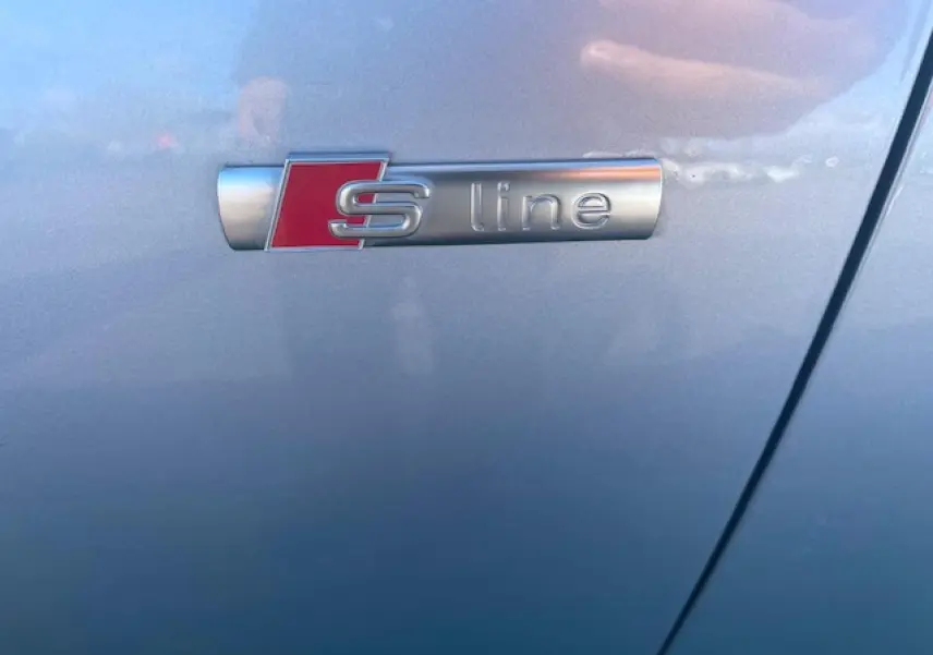 Gros plan sur l'emblème S line argent et rouge sur la porte côté gauche d'une Audi A4 argent fleuret métal.