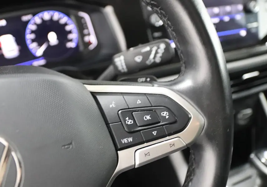Gros plan sur le volant noir de la Volkswagen Polo 2022 avec commandes multifonctions et affichage digital du tableau de bord flou.