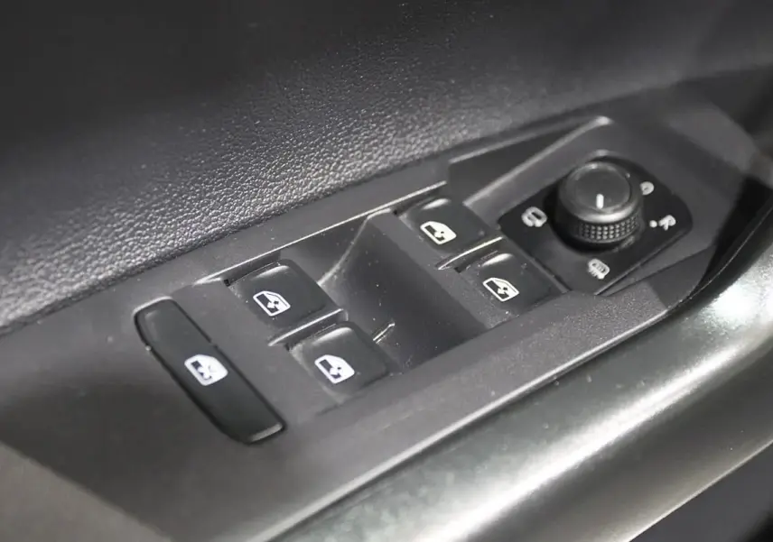 Gros plan sur les commandes électriques des vitres et rétroviseurs côté conducteur d'une Volkswagen Polo noire 2022.