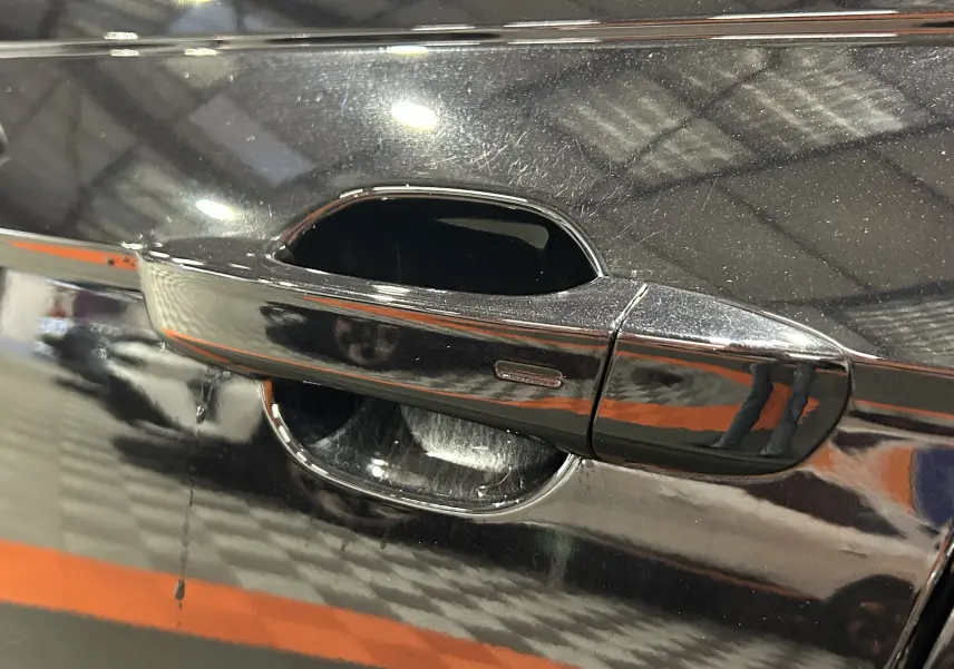 Poignée de porte côté gauche noire brillante d'une Volkswagen Polo 2022, reflet d'un intérieur d'entrepôt visible.