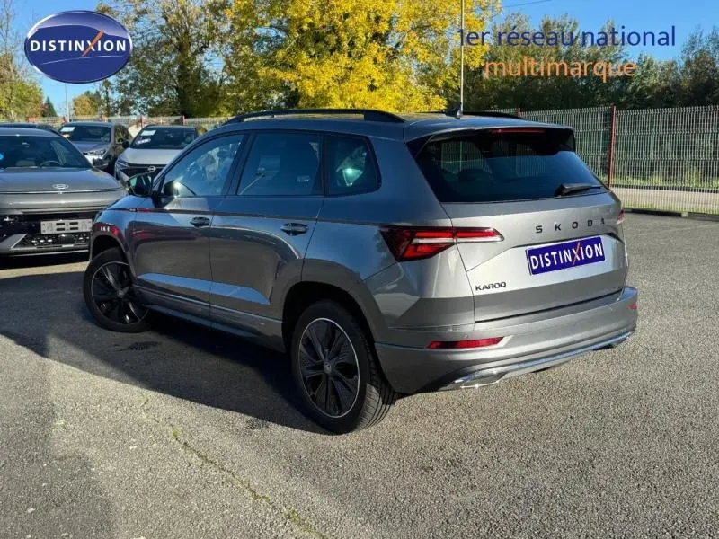 Vue 3/4 arrière droite d'un Skoda Karoq gris perle avec jantes alu et barres de toit, stationné en extérieur.
