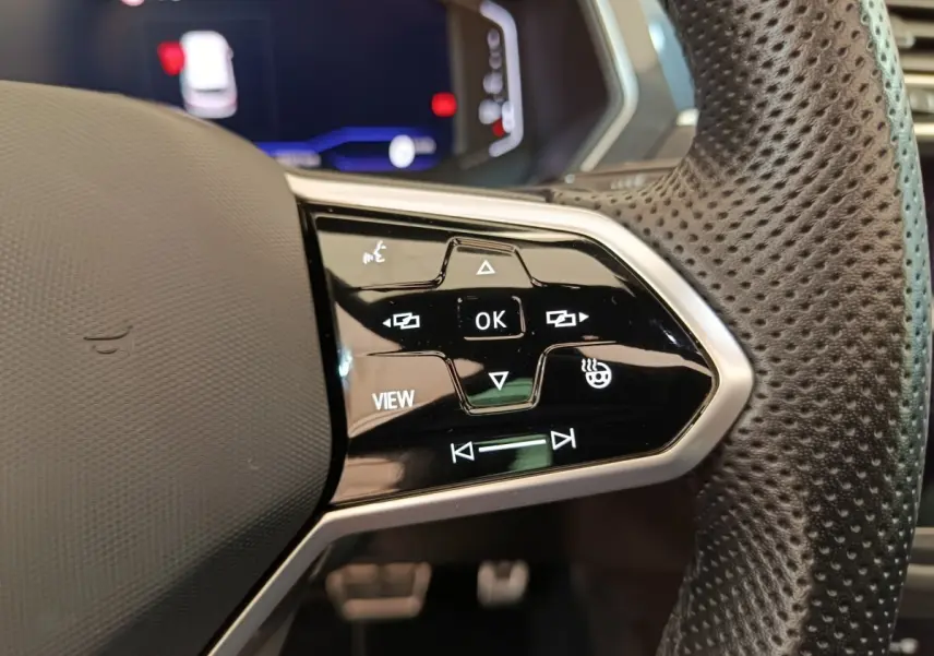 Gros plan sur les commandes à droite du volant cuir perforé du Volkswagen Tiguan noir, affichage numérique en arrière-plan.