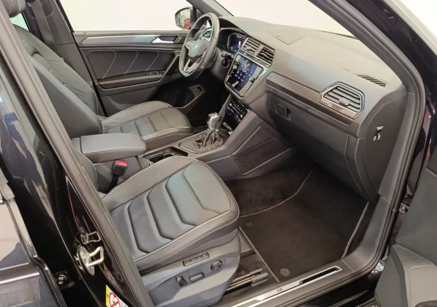 Vue intérieure côté conducteur du Volkswagen Tiguan noir 1.4 eHybrid 2023 avec sièges cuir et tableau de bord digital.