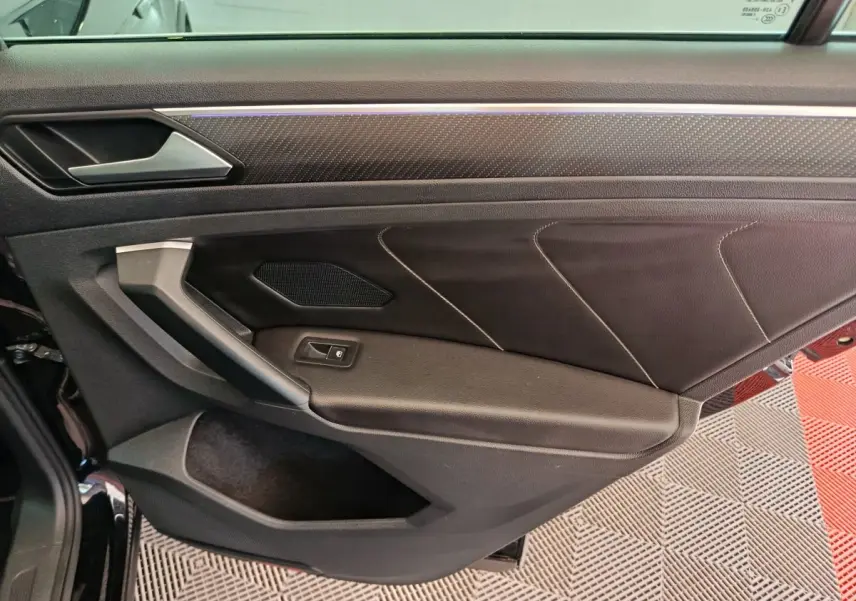 Vue intérieure côté gauche de la porte avant noire du Volkswagen Tiguan 2023 avec garniture cuir et bouton de vitre électrique.