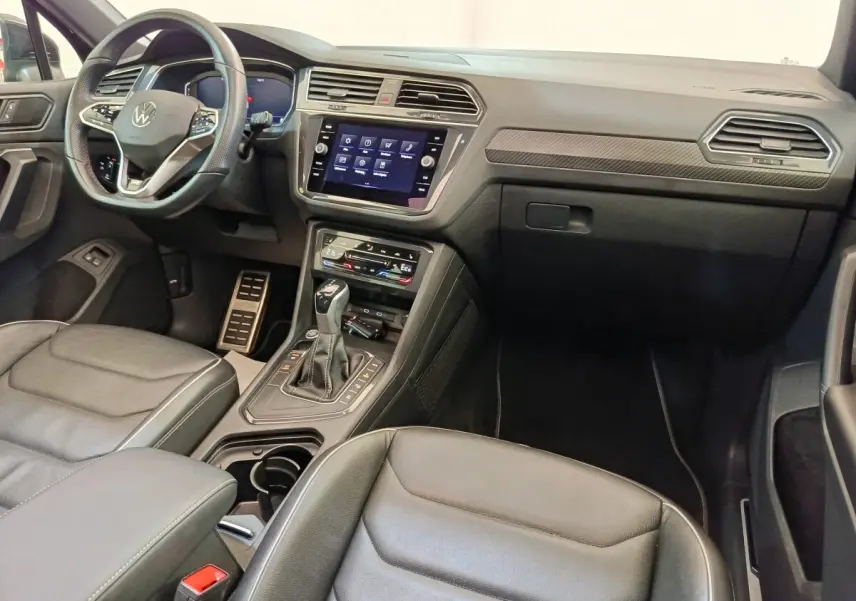 Vue intérieure avant droite du Volkswagen Tiguan 1.4 eHybrid 2023, tableau de bord noir avec écran tactile central et volant cuir multifonctions.