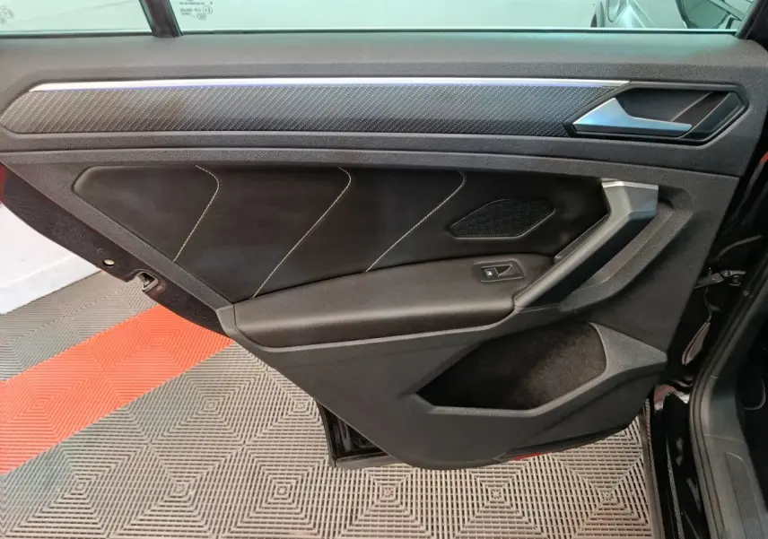 Vue intérieure de la porte arrière droite noire du Volkswagen Tiguan 1.4 eHybrid 2023 avec surpiqûres blanches et insert carbone.