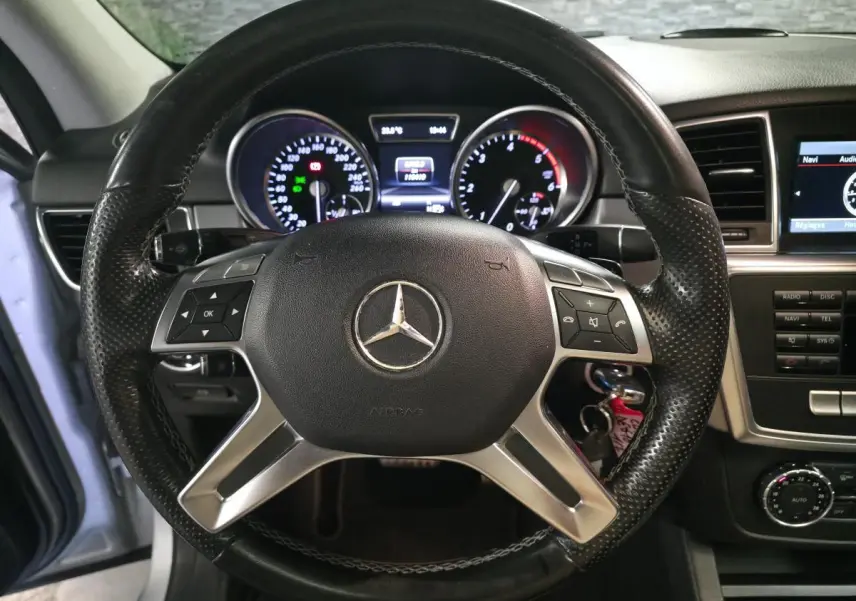 Vue intérieure centrée sur le volant cuir noir perforé et le tableau de bord du Mercedes Classe M gris, 2014.