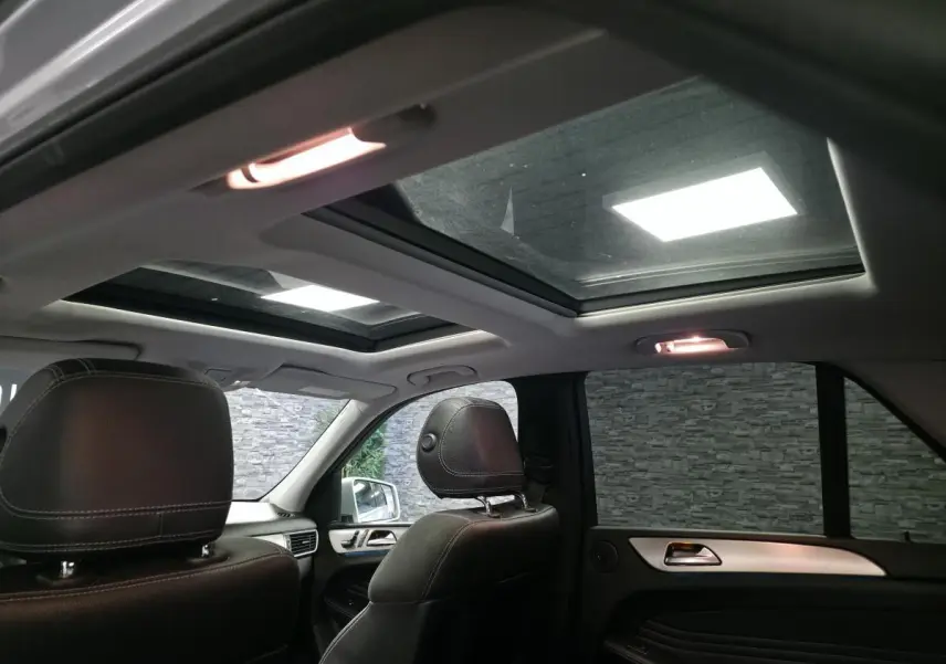Vue intérieure arrière du Mercedes Classe M gris, mettant en valeur le toit ouvrant panoramique en verre et les sièges cuir noirs.