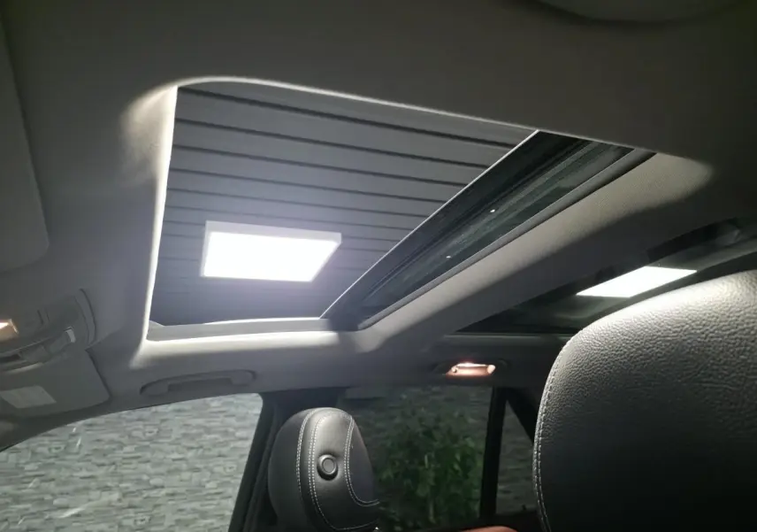 Vue intérieure du toit ouvrant panoramique électrique en verre du Mercedes Classe M gris, avec sièges en cuir noir visibles.