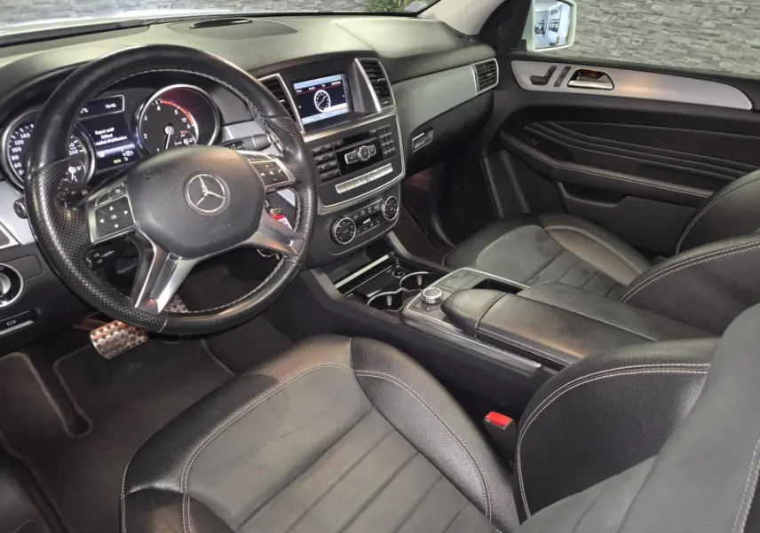 Vue intérieure côté conducteur de la Mercedes Classe M ML 350 BlueTEC 2014 avec tableau de bord noir et volant cuir perforé.