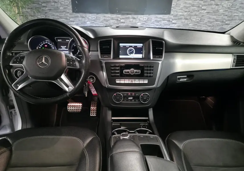 Vue intérieure avant de la Mercedes Classe M 350 BlueTEC 2014, tableau de bord noir avec volant cuir multifonctions et écran central.