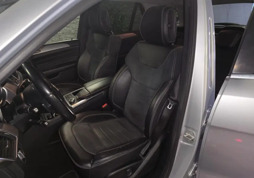 Vue intérieure côté conducteur du Mercedes Classe M gris, sièges en cuir noir avec surpiqûres blanches et console centrale.