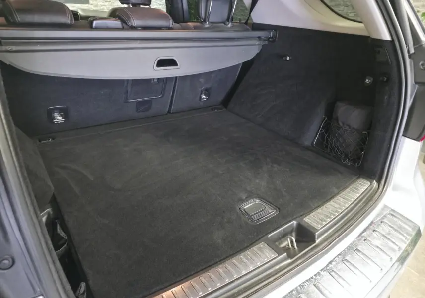 Coffre ouvert vu de l'arrière d'un Mercedes Classe M gris avec cache-bagages et tapis noir.