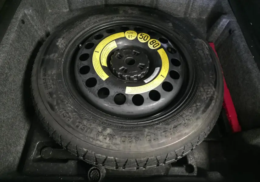 Gros plan sur la roue de secours galette noire dans le coffre d’un Mercedes Classe M gris.