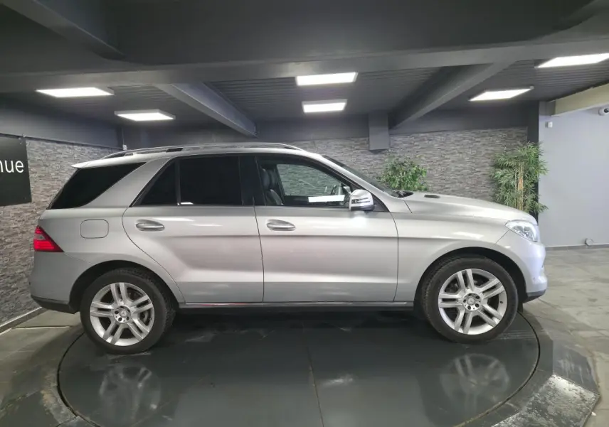 Vue de profil côté gauche d’un Mercedes Classe M gris métallisé avec jantes alliage 5 branches doubles et vitres teintées.