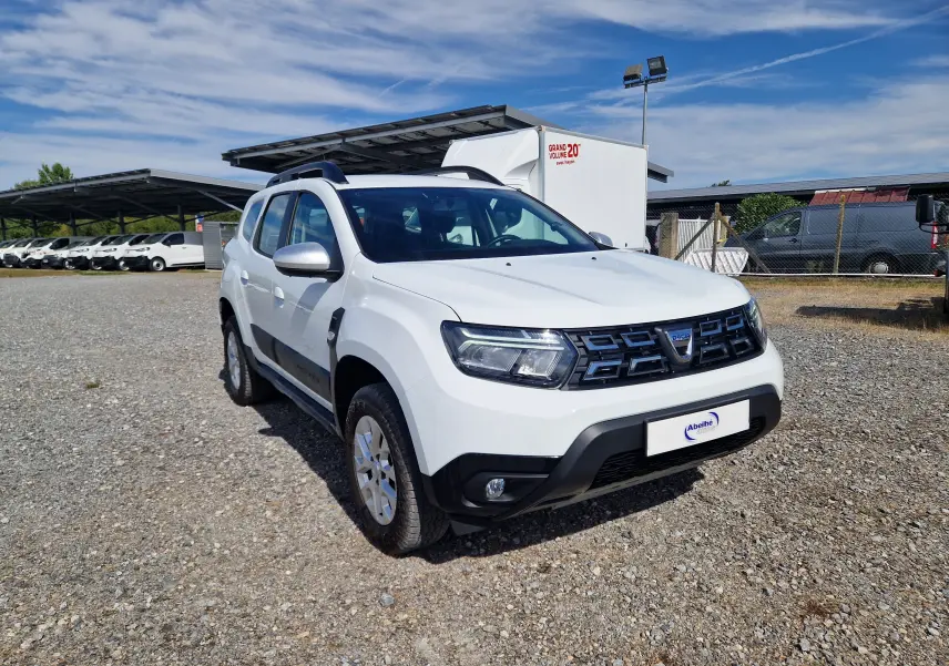 Dacia Duster blanc en 3/4 avant droit, SUV 4x4 avec calandre noire et protections noires sur les bas de caisse.