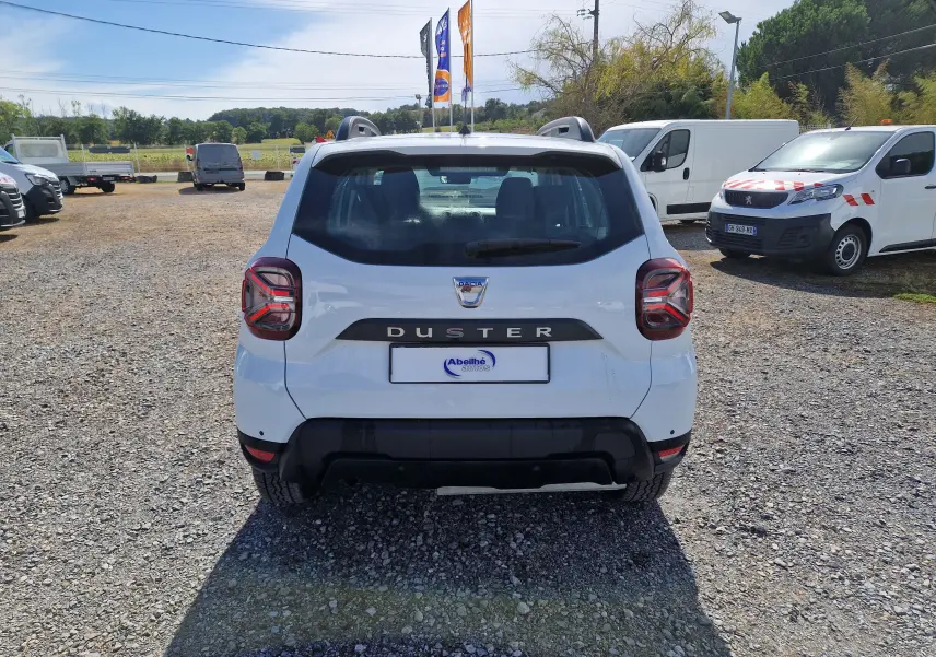 Vue arrière d'un Dacia Duster blanc 2023, avec logo et nom du modèle bien visibles sur un terrain extérieur.