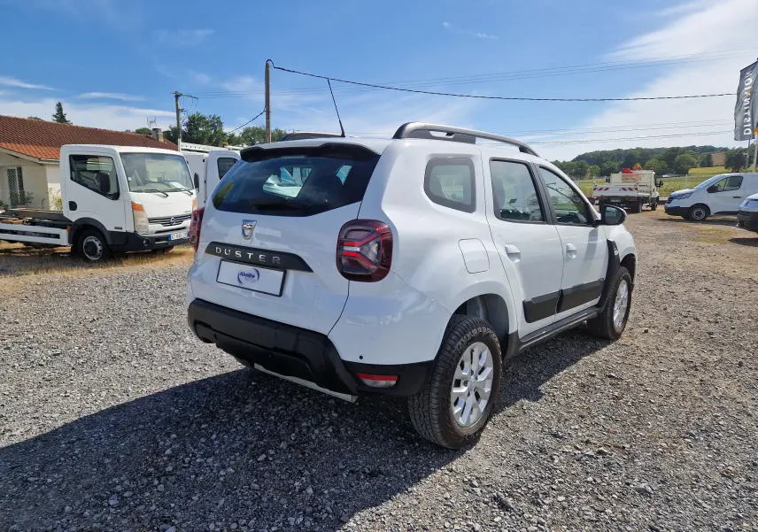 Vue 3/4 arrière droite du Dacia Duster blanc 4x4 2023 avec protections noires et jantes alliage 16 pouces.
