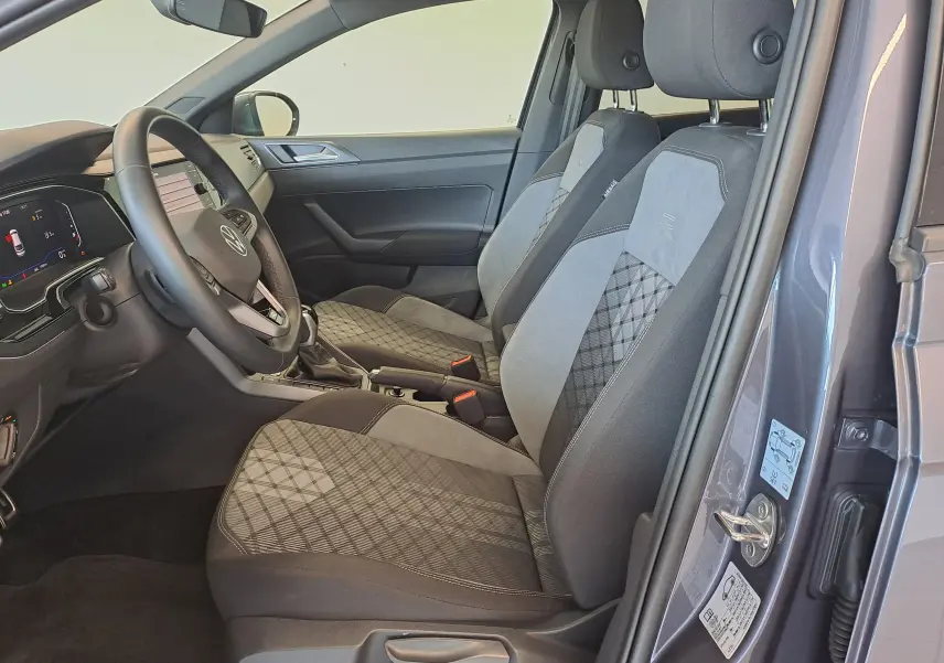 Vue intérieure côté conducteur de la Volkswagen Taigo gris cendre 2025, sièges tissu avec motifs géométriques et volant multifonction.