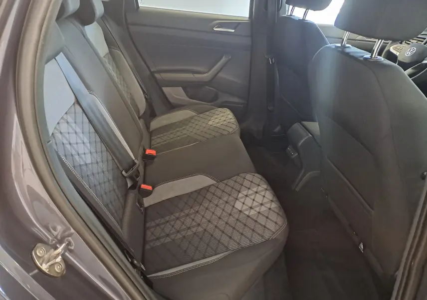 Vue intérieure arrière gauche du Volkswagen Taigo 2025 gris cendre, sièges tissu à motifs géométriques et ceintures de sécurité visibles.
