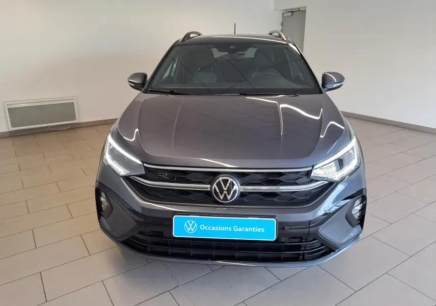 Vue avant d'un Volkswagen Taigo gris cendre 2025 en finition R-Line, avec calandre noire et phares LED allumés.