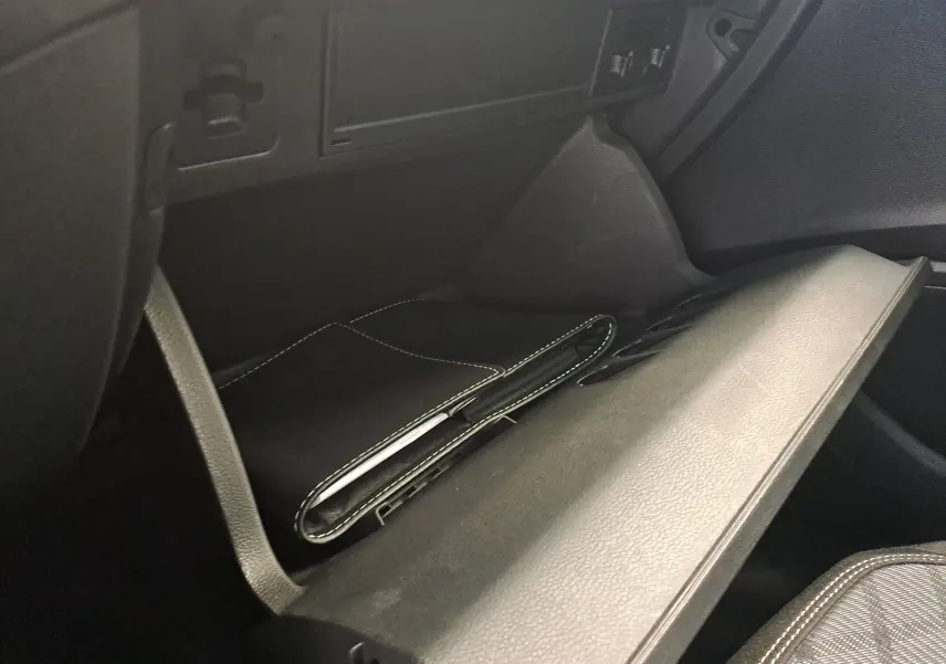 Gros plan de la boîte à gants ouverte du Volkswagen Taigo gris cendre, montrant un porte-documents noir à l'intérieur.