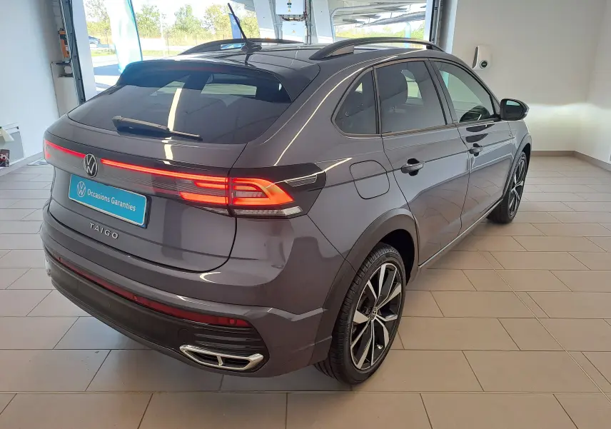 Vue 3/4 arrière droite du Volkswagen Taigo gris cendre avec feux arrière allumés et jantes alliage 18 pouces Misano.