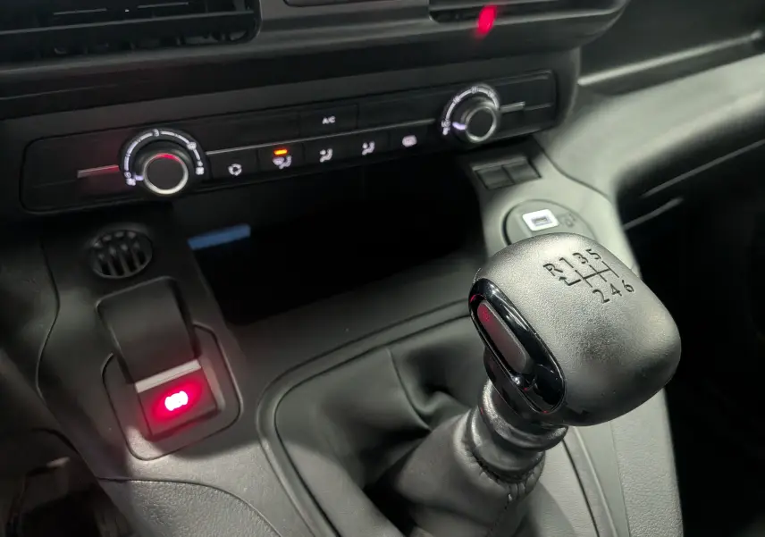 Gros plan sur le levier de vitesses manuel noir du Citroën Berlingo blanc, avec les commandes de climatisation en arrière-plan.