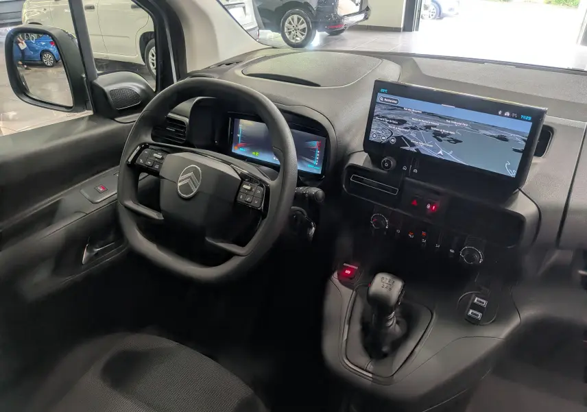 Intérieur du Citroën Berlingo 2025 blanc, vue côté conducteur, tableau de bord avec écran tactile et boîte manuelle.