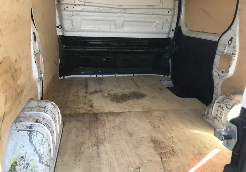 Intérieur du fourgon Renault Trafic blanc vu de l'arrière, montrant la zone de chargement avec revêtement en bois usé.